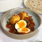 Kerala Egg Roast on a plate, one egg cut in half and chapati's in the background.