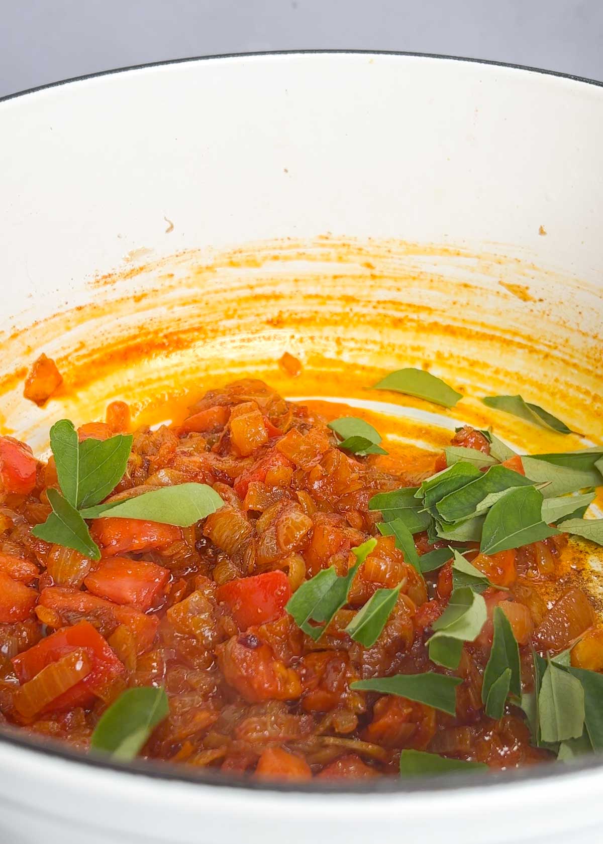 torn curry leaves added into pot of caramelised tomato and onions with authentic spices