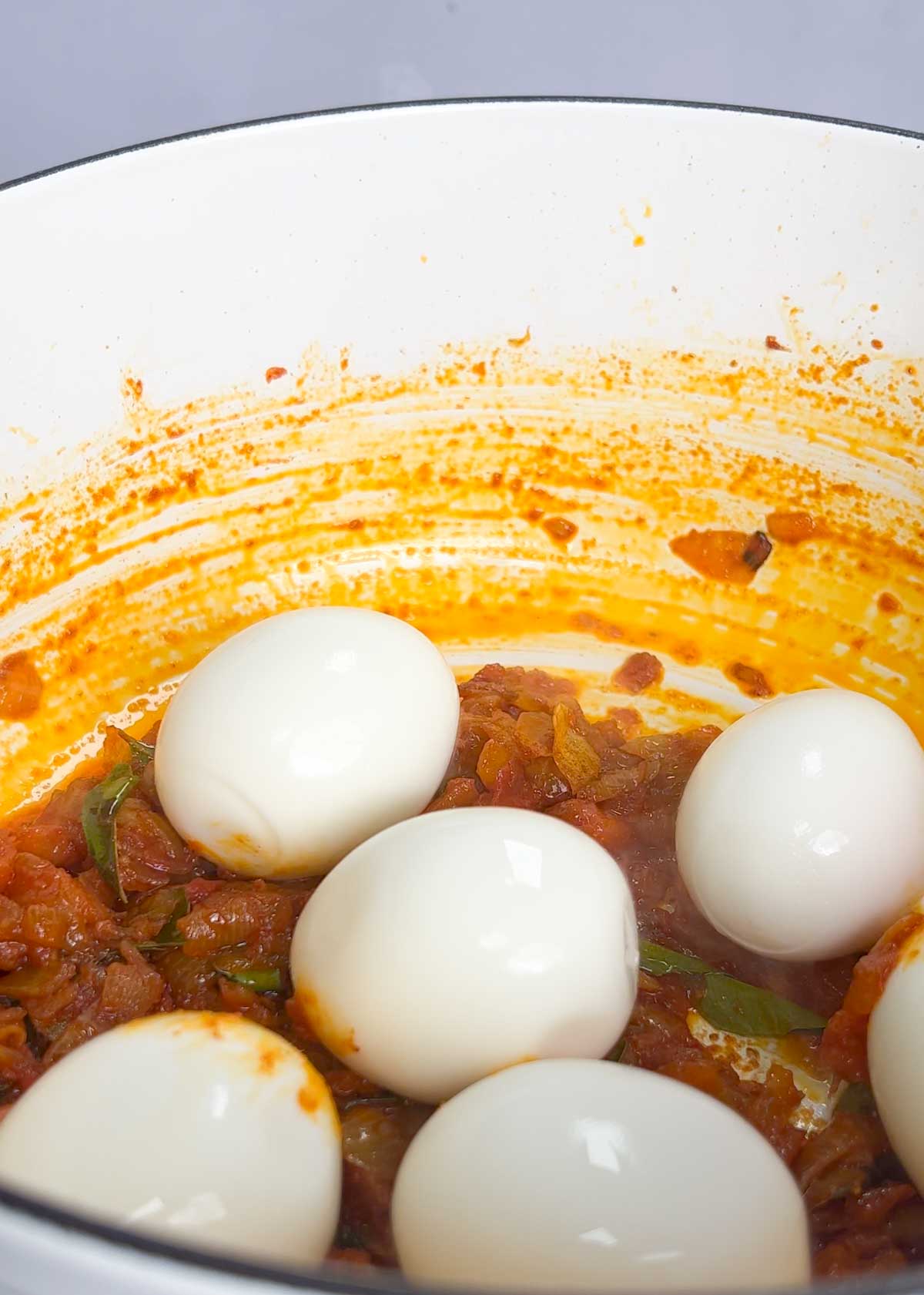 boiled eggs added in pot of caramelised onions and tomatoes that have been lightly spiced