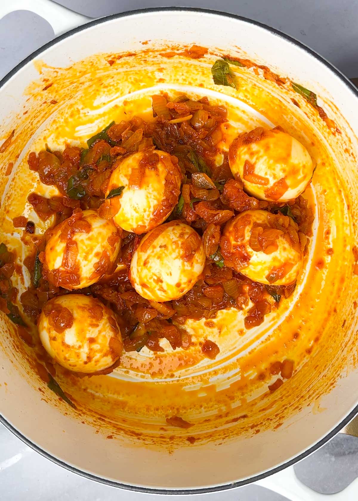 white pot containing finished dish of kerala style egg roast, boiled eggs coated in caramelised onions and tomatoes that have been lightly spiced