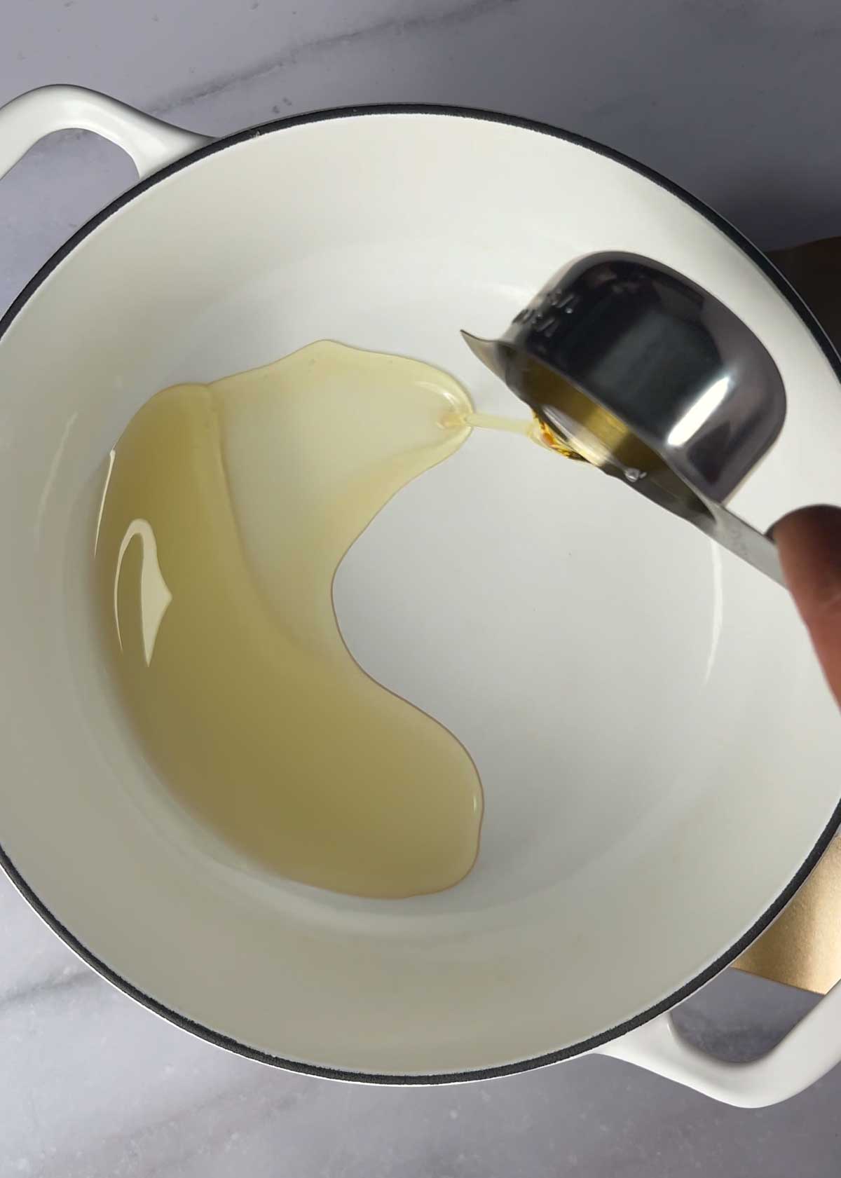 pouring oil into a white cast iron dutch oven