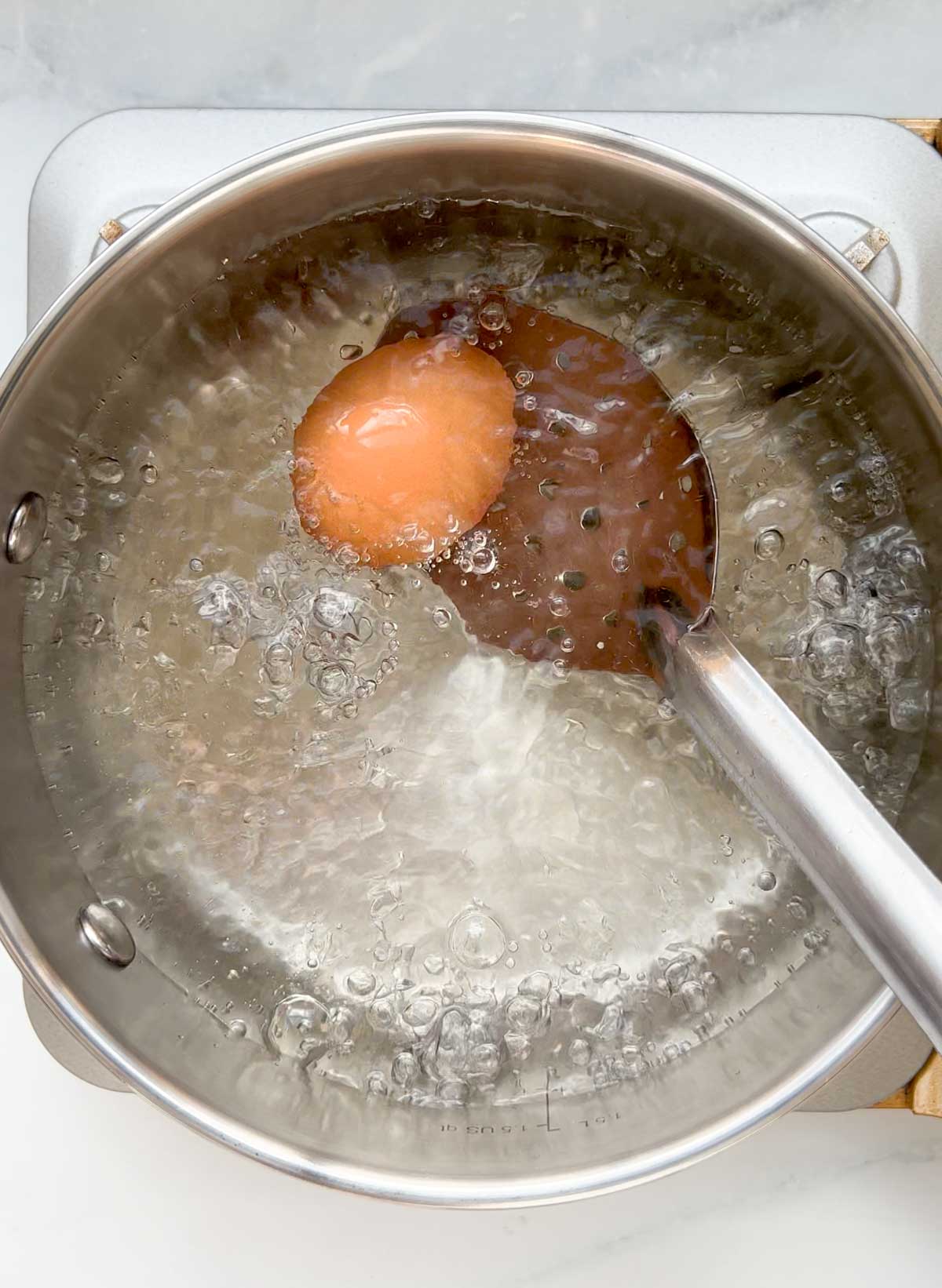 gently lowering an egg into boiling water with a slotted spoon