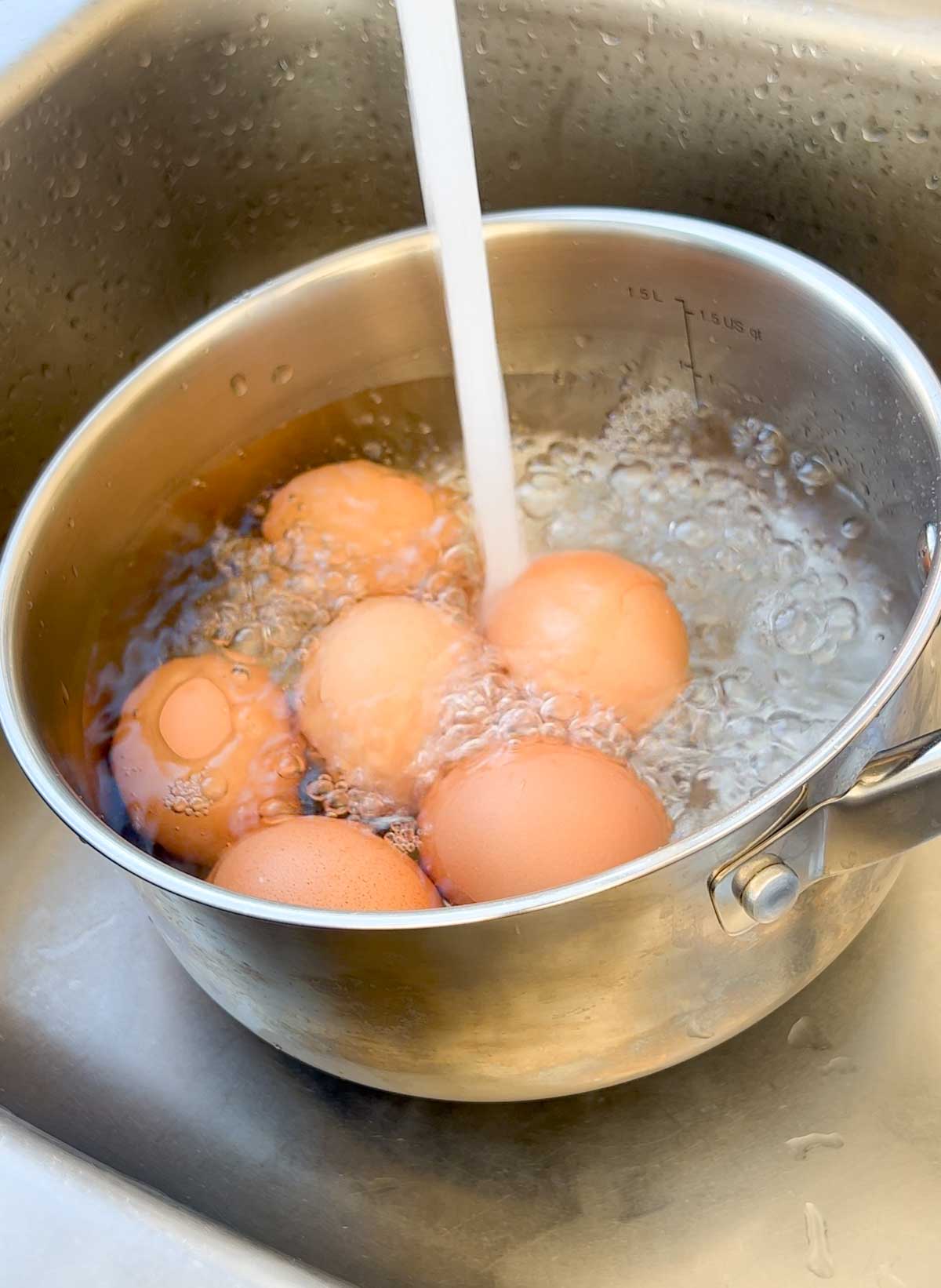 running cold tap water over boiled eggs in a pot