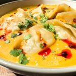 Jhol Achar Chicken Momo served on a plate topped with sesame seeds, chopped coriander and chilli oil
