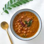 bowl of black chickpeas curry or kadala curry with a golden spoon beside it and a sprig of curry leaves