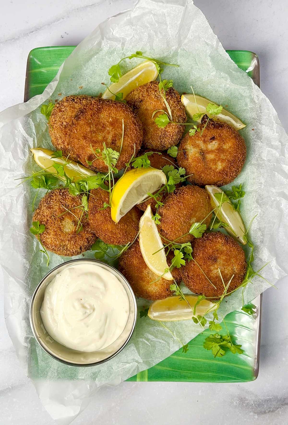 Crispy Kerala tuna fish cutlets (patties) served on a platter with lemon wedges, fresh coriander, and tartare sauce.