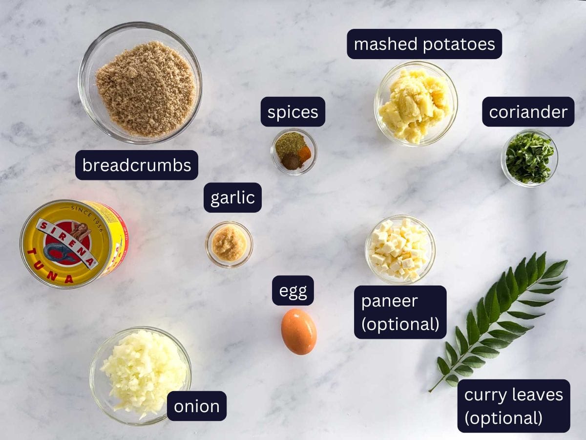 top view of ingredients needed to make easy kerala tuna fish cutlets (patties) breadcrumbs, spices, garlic, onion, tuna, egg, mashed potatoes, coriander, paneer and curry leaves.