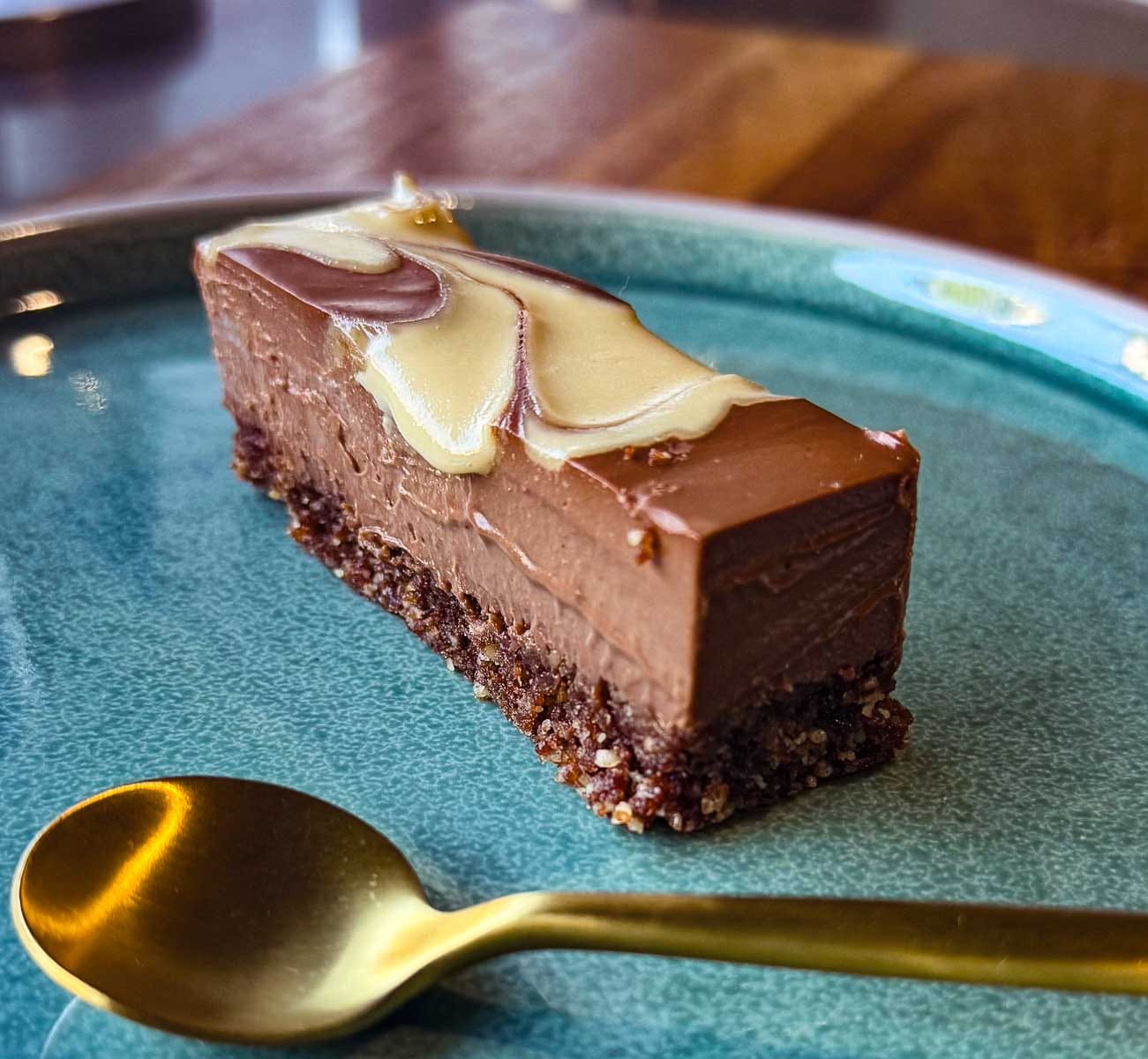 Healthy chocolate mousse bar with a smooth, creamy topping and nutty base, served on a ceramic plate with a gold spoon.