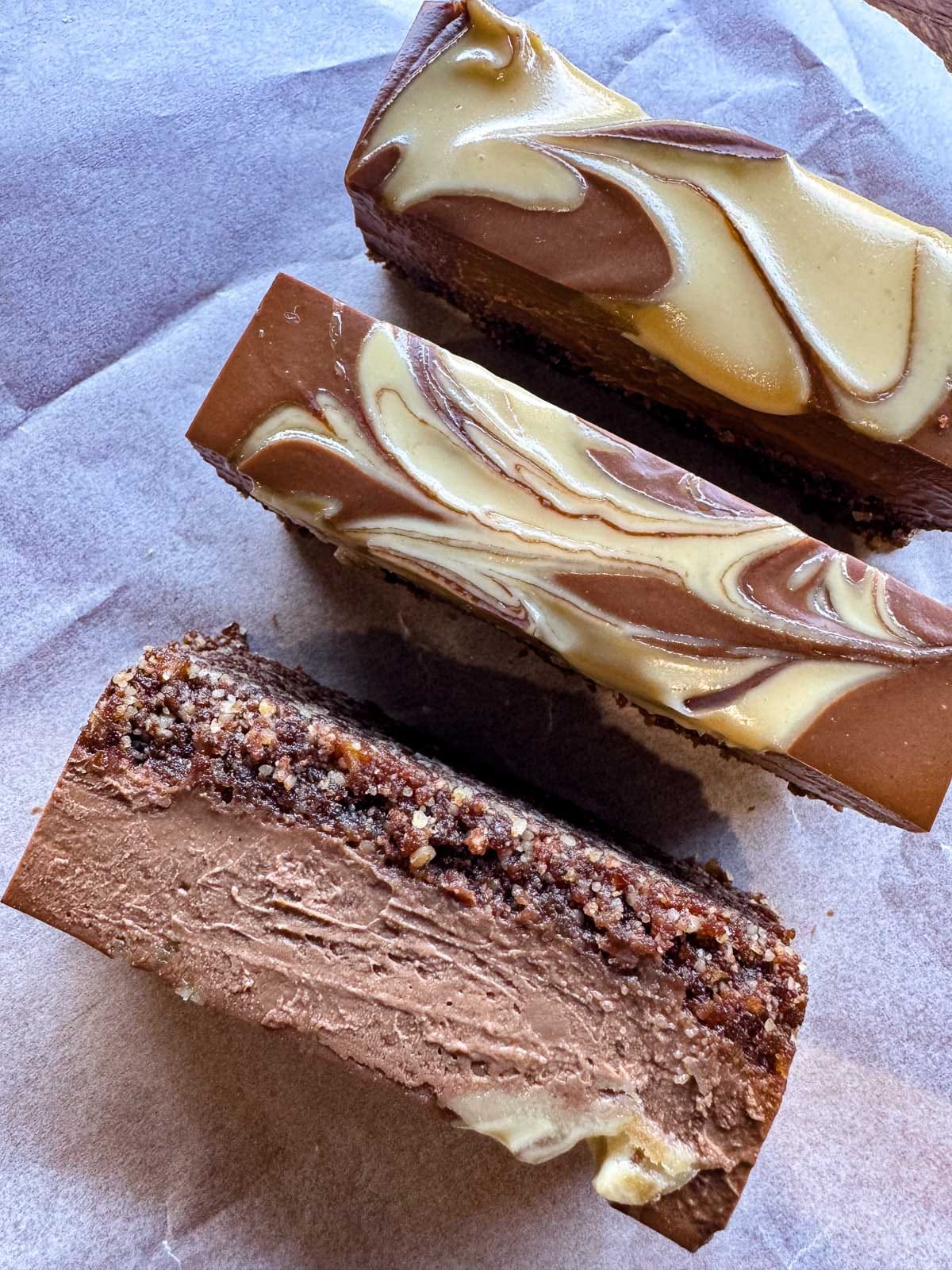 Close-up of sliced healthy chocolate mousse bars with a creamy tahini swirl topping on parchment paper.
