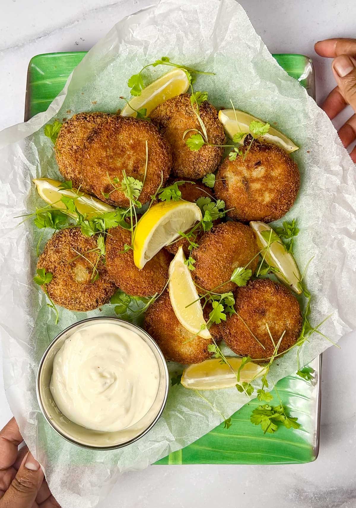Crispy Kerala tuna fish cutlets (patties) served on a platter with lemon wedges, fresh coriander, and tartare sauce.