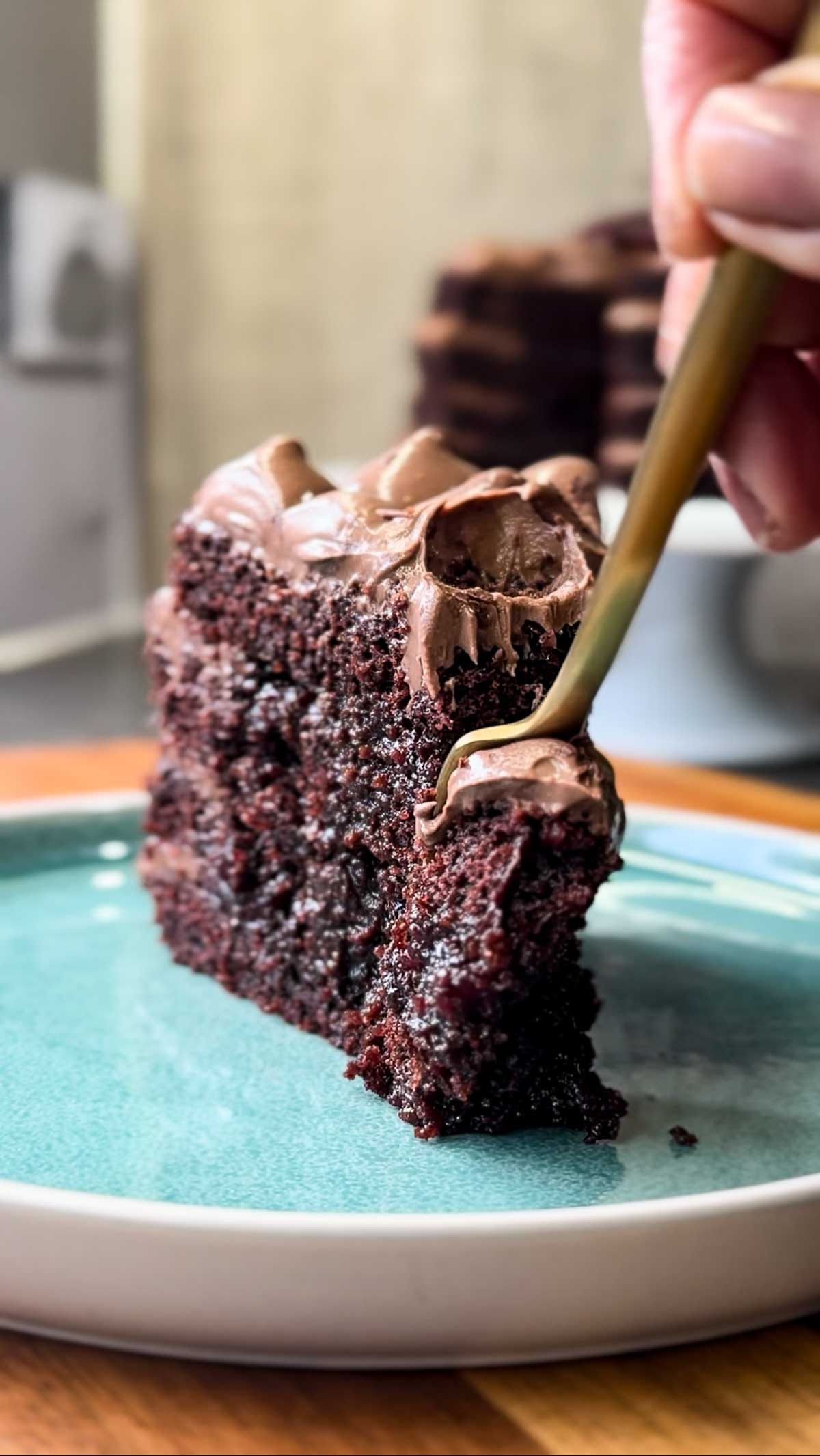 Close-up of a slice of Moist Chocolate Cherry Cake with cherry jam and chocolate custard cream frosting, fork taking a bite