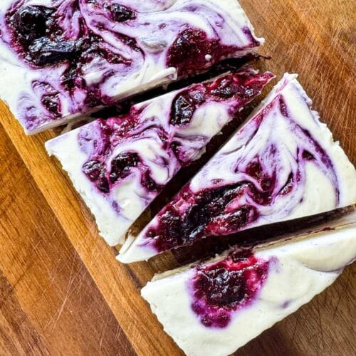 vegan no bake cheesecake with blueberry swirls on top. sliced into triangles on a wooden board