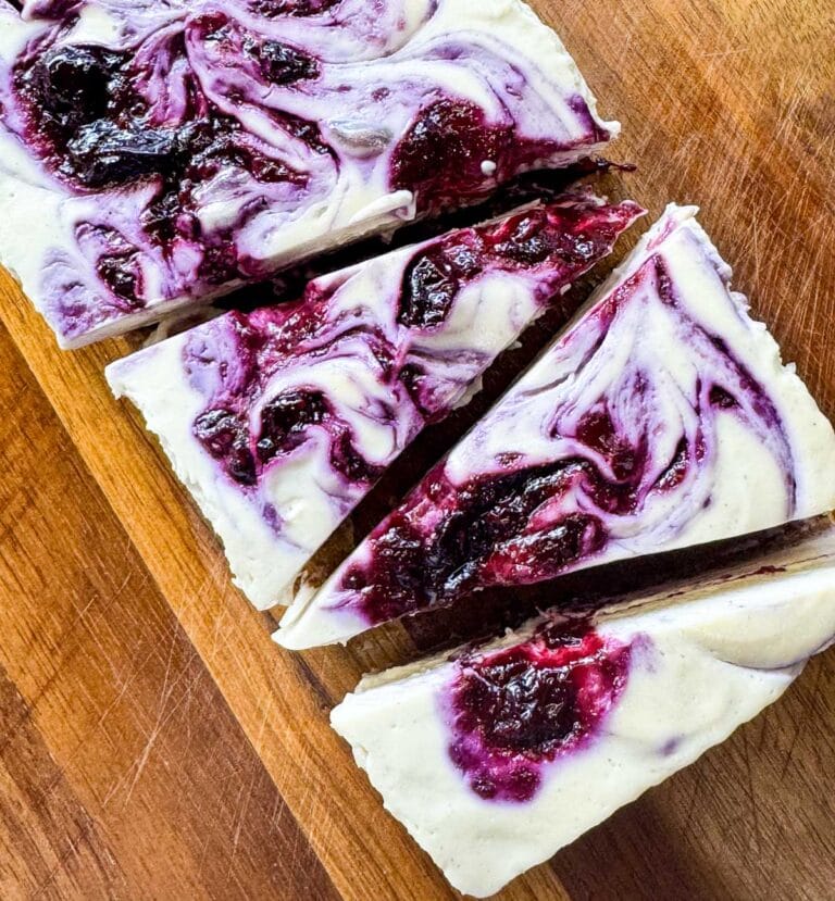 vegan no bake cheesecake with blueberry swirls on top. sliced into triangles on a wooden board