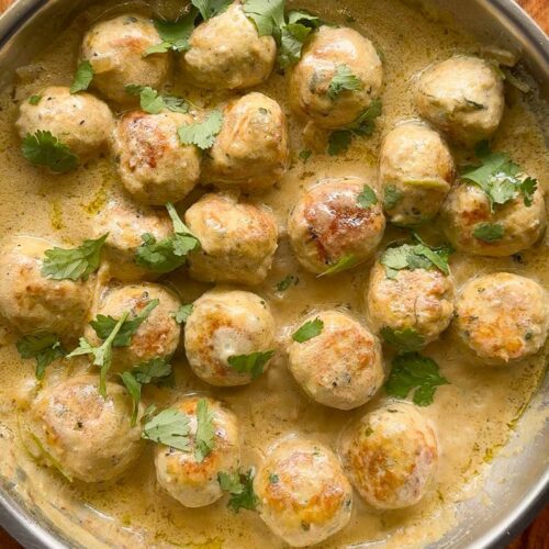 creamy chicken kofta curry in a pan, with wooden background