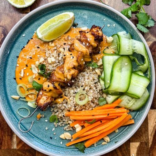 satay chicken skewer on bed of quinoa, on a blue plate with wedge of lime, cucumber ribbons, carrot