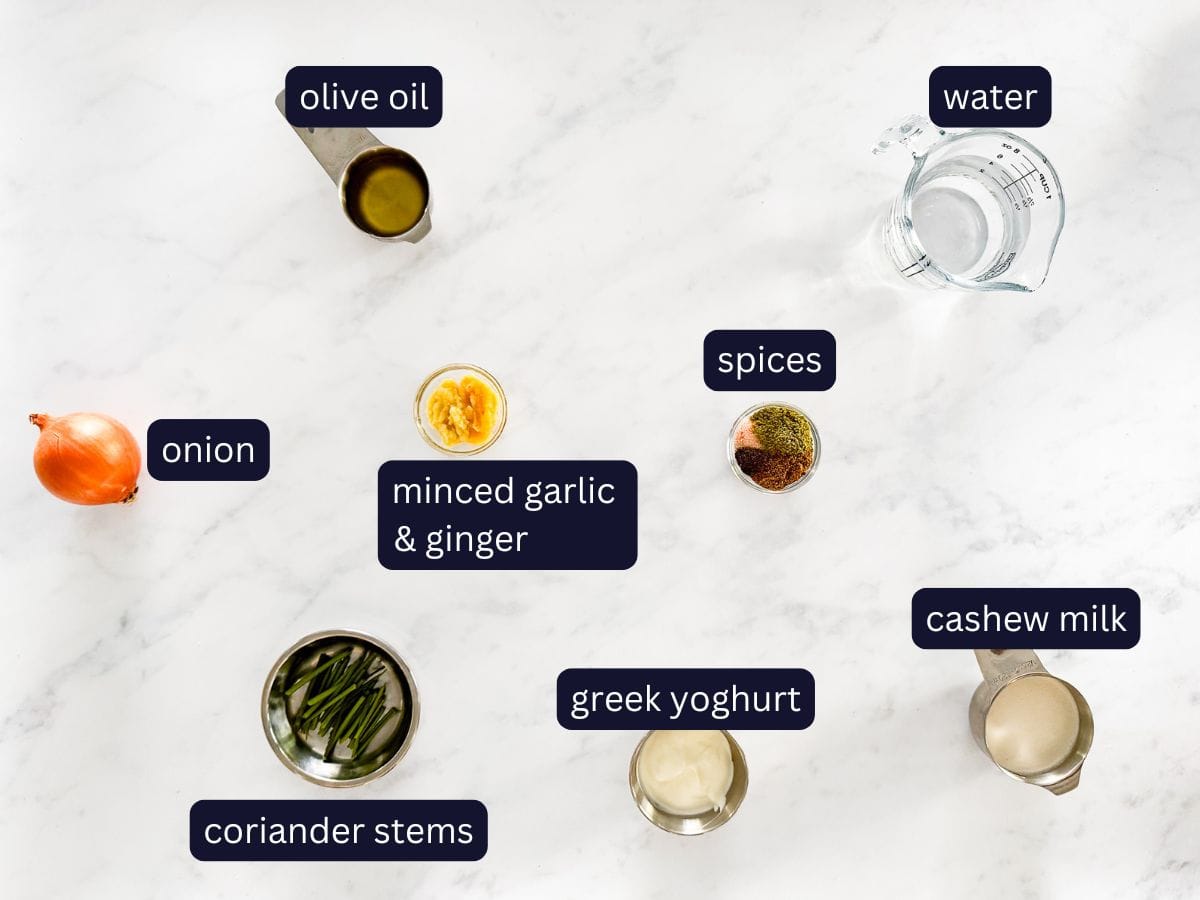 Ingredients to make the curry for.. on a Marble background, including, onion, olive oil, minced garlic &* ginger, coriander stems, greek yoghurt, cashew milk, spices, and water.