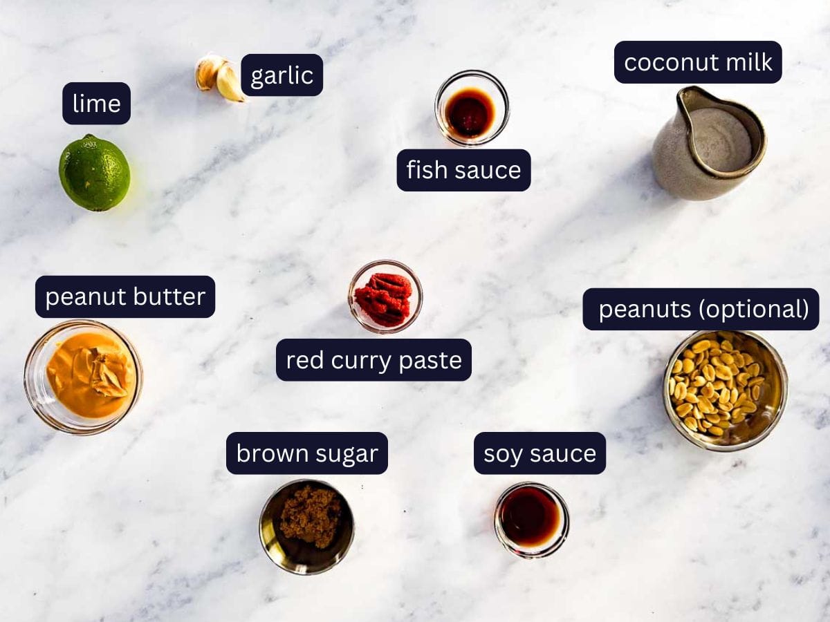 top shot on marble background of ingredients for the peanut sauce that goes with the air fryer satay chicken skewers. including coconut milk, red curry paste, fish sauce, sou sauce, garlic, brown sugar lime, peanuts and spices.