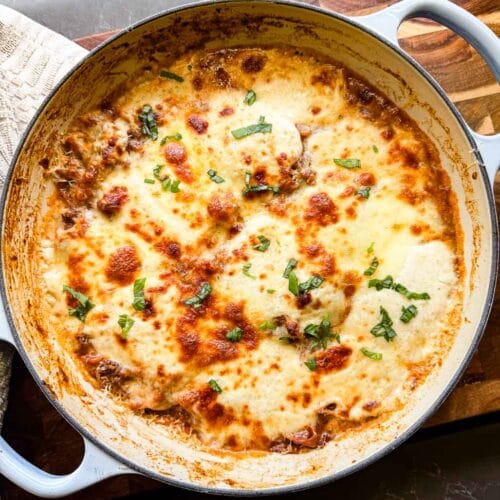 cooked lasagna in le creuset dutch oven skillet with a wooden background