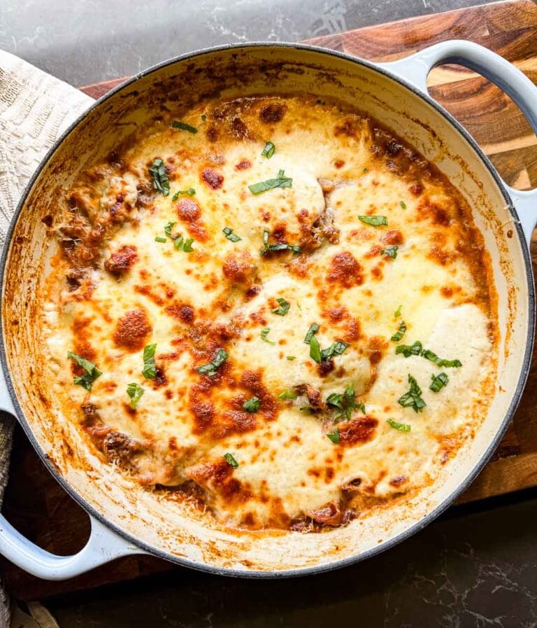 cooked lasagna in le creuset dutch oven skillet with a wooden background