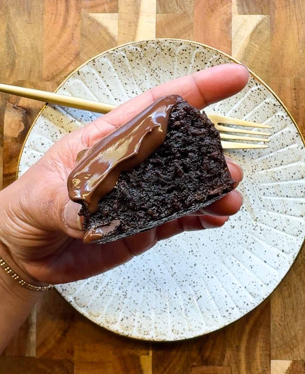 hold handling a slice of the best healthy frosted almond flour brownie. speckled plate and fork in the background