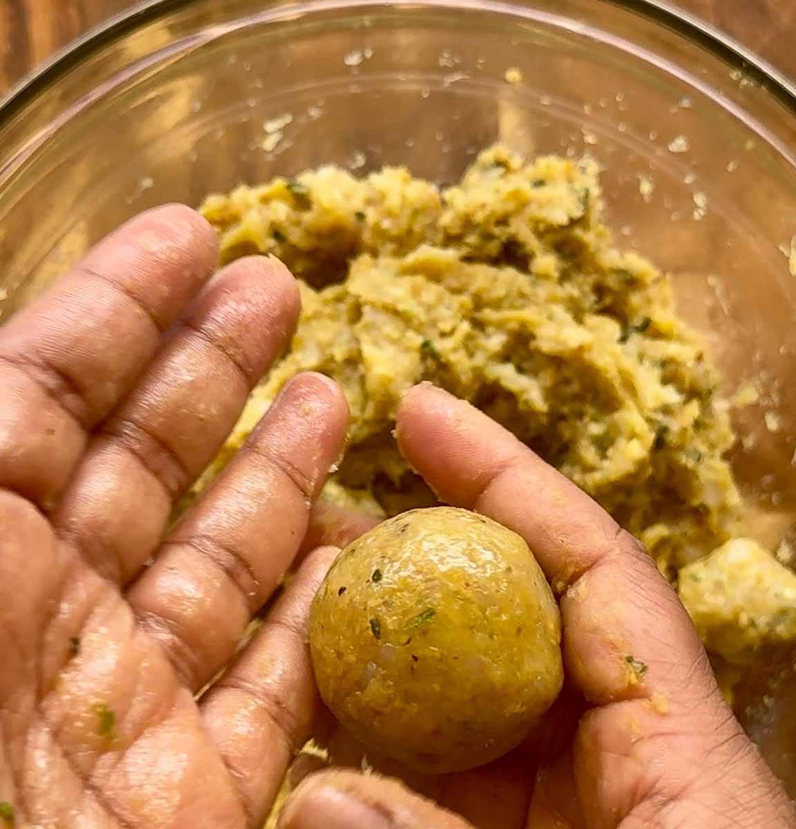 rolled meatball being held in a hand with remaining mixture in a bowl in the background.